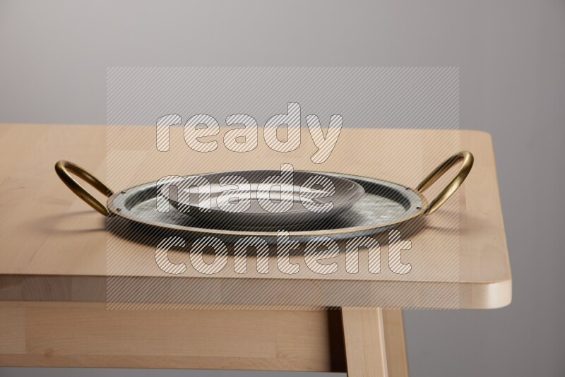 white plate placed on a rounded stainless steel tray with golden handels on the edge of wooden table