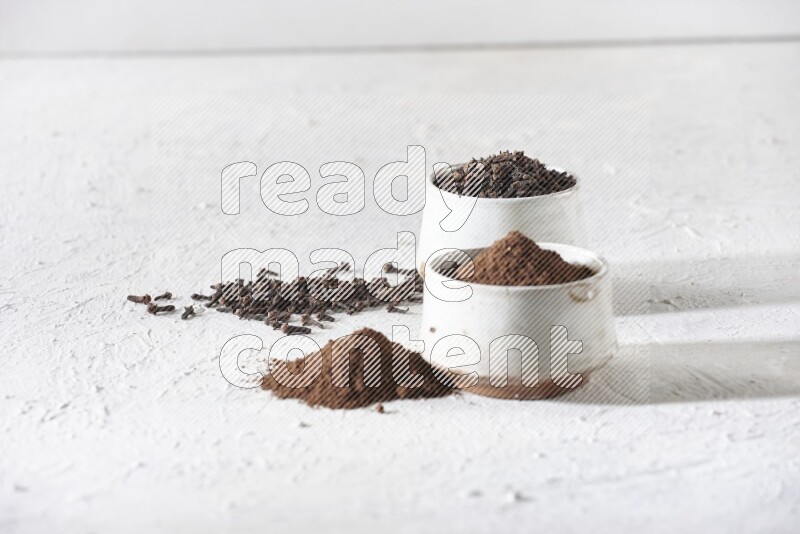 2 Beige ceramic bowls, one full of cloves and the other full of powder on textured white flooring