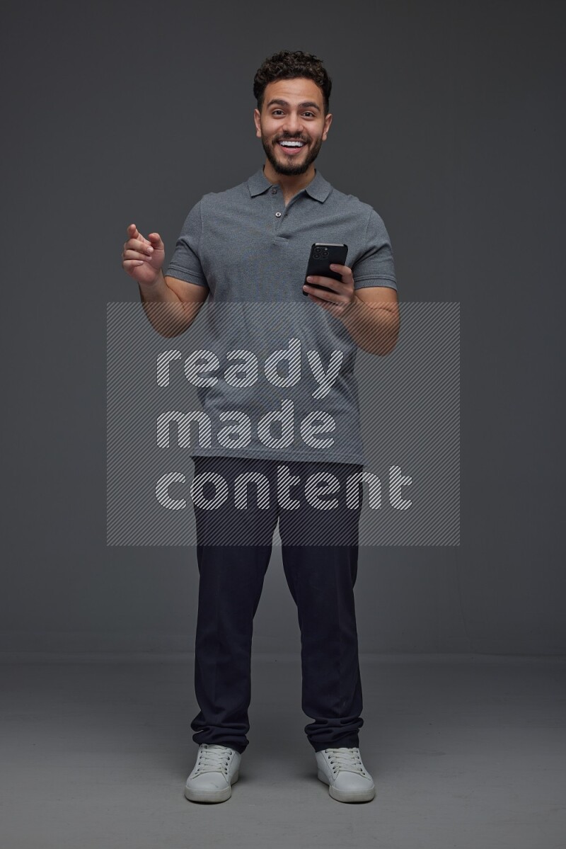 A man wearing casual standing and using his phone and making multi hand gestures eye level on a gray background
