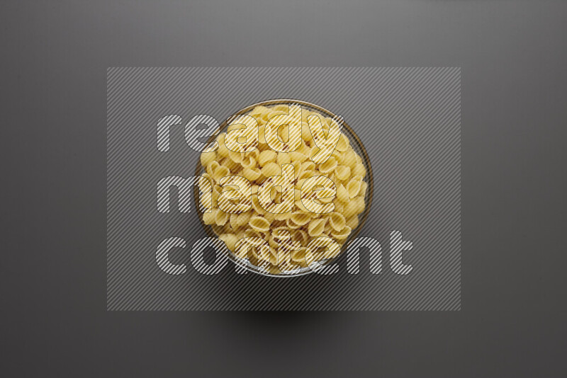 Shells pasta in a glass bowl on grey background