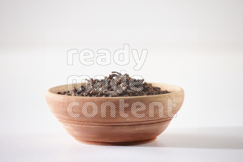 A wooden bowl full of cloves on a white flooring