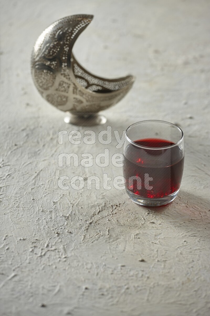 A silver lantern with different drinks, dates, nuts, prayer beads and quran on textured white background