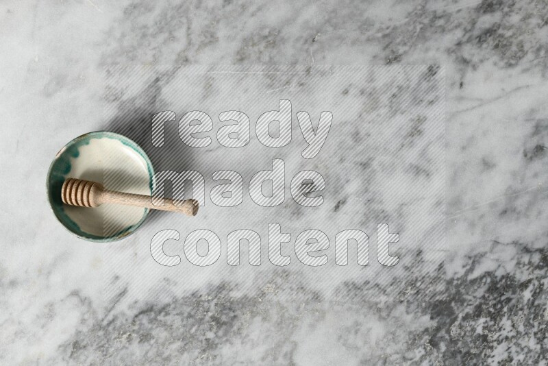 وعاء فخاري متعدد الألوان مع ملعقة عسل خشبية بداخله على خلفية من الرخام الرمادي