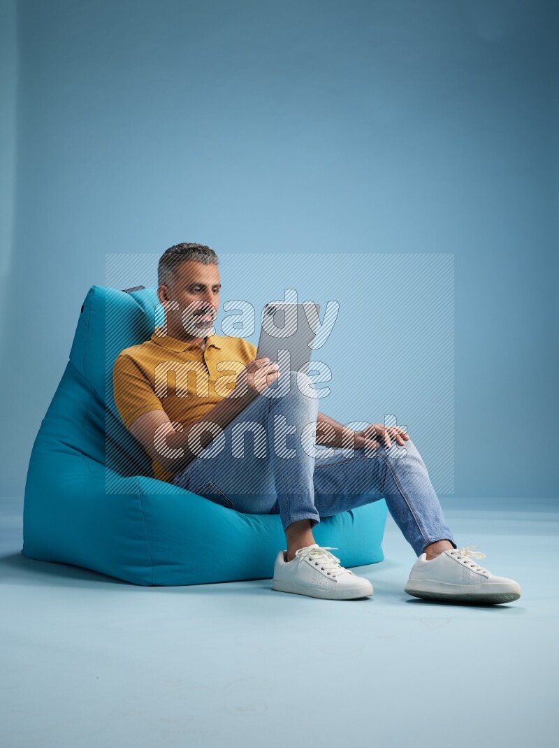 A man sitting on a blue beanbag and working on tablet