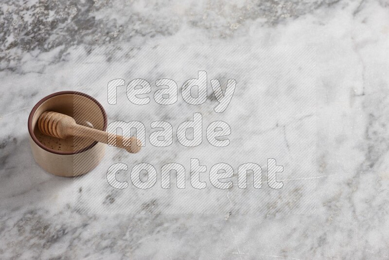 Beige Pottery oven bowl with wooden honey handle on the side with grey marble flooring, 65 degree angle