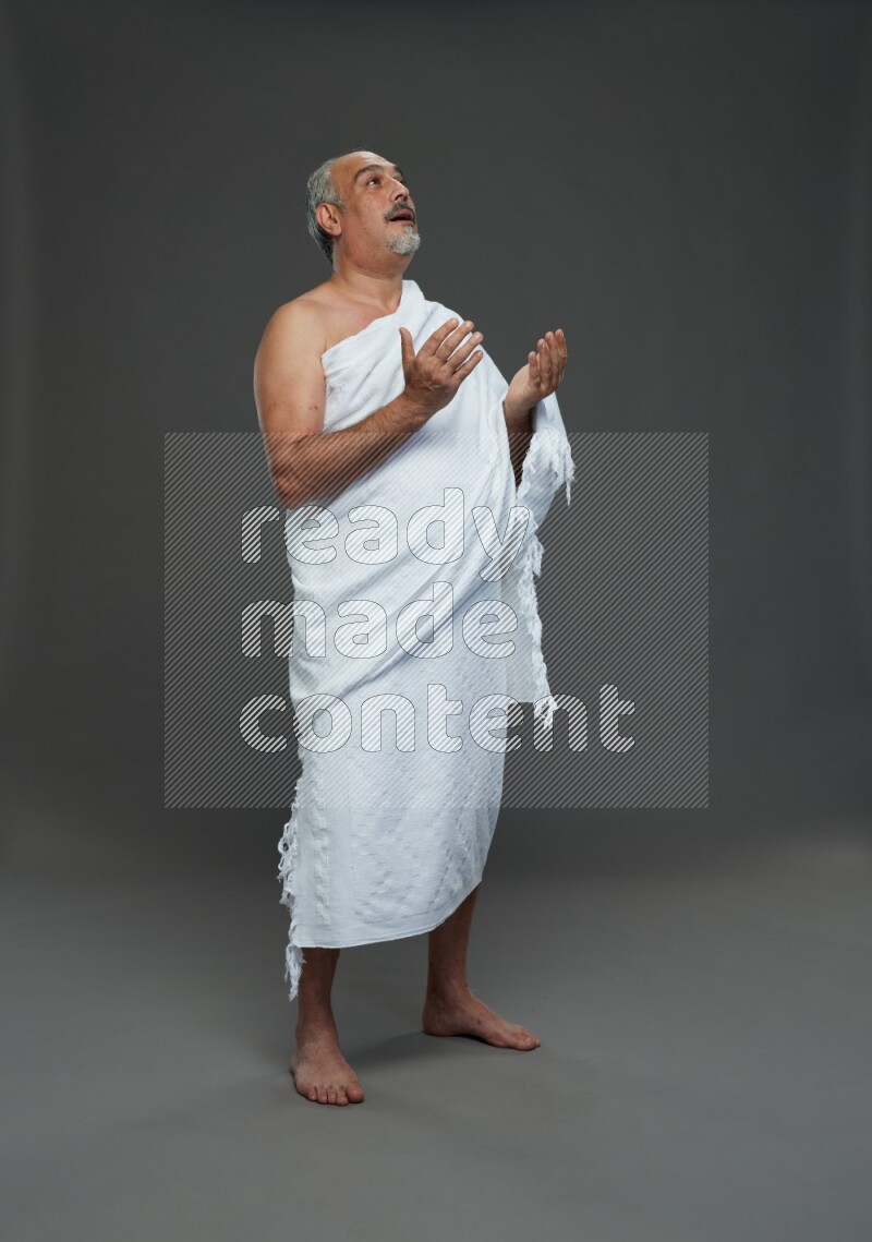 A man wearing Ehram Standing dua'a on gray background
