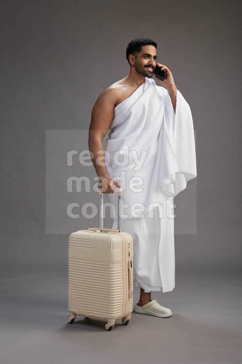 A man wearing Ehram Standing holding traveling bag on gray background