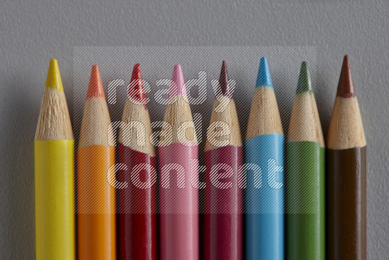 A collection of colored pencils arranged showcasing a gradient of different hues on grey background