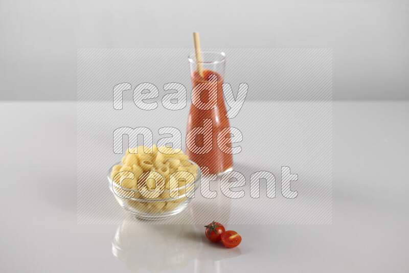 Raw pasta with tomatoe pasta with different ingredients such as cherry tomatoes, basil, garlic, bay laurel, cardamom, white pepper, black pepper, red chilis and wheat stalks on light grey background