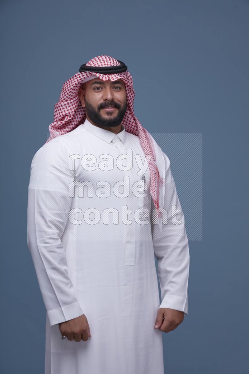 A Saudi man posing on blue background wearing Thob and Shomag