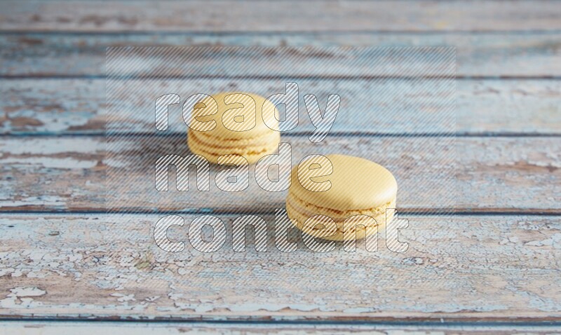 45º Shot of two Yellow Vanilla macarons on a light blue wooden background