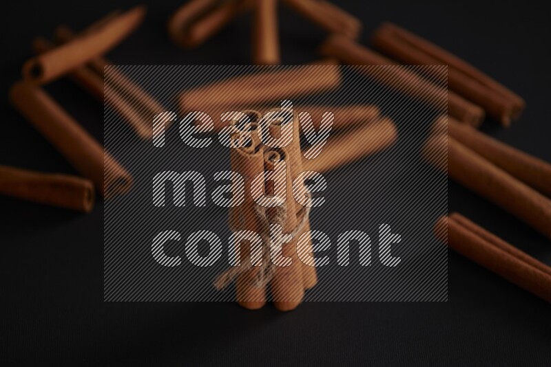 4 Cinnamon sticks stacked and bounded with more sticks in the background on black flooring