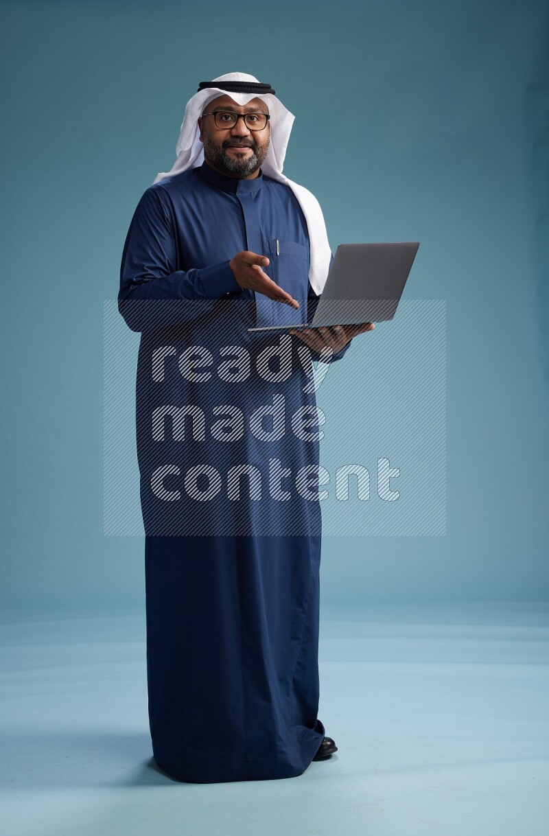Saudi Man with shimag Standing working on laptop on blue background