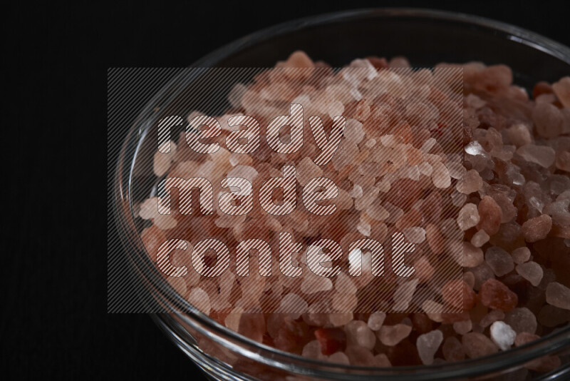A glass bowl full of coarse himalayan salt crystals on black background