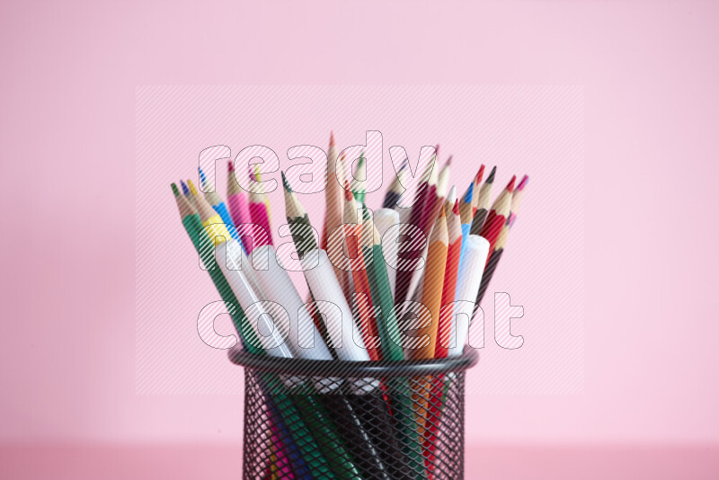 Pens, pencils and other different school supplies in a metal pen holder on rose background