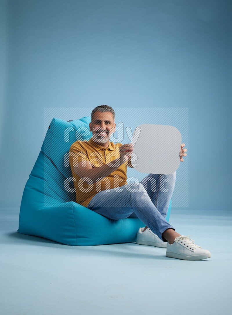 A man sitting on a blue beanbag and holding social media sign