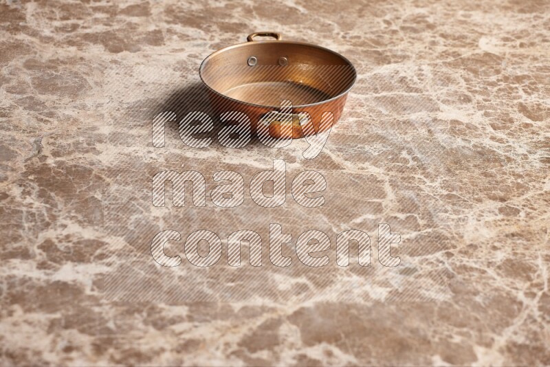 A small copper pan on beige marble background