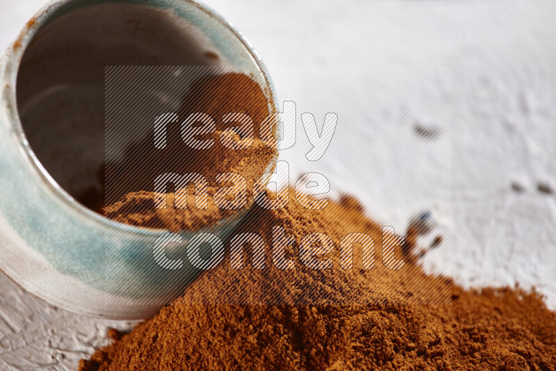 A colored pottery bowl full of ground paprika powder with fallen powder from it on white background