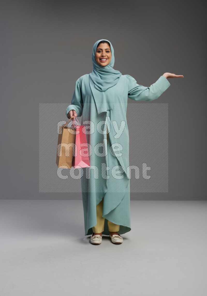 Saudi Woman wearing Abaya standing holding shopping bag on Gray background