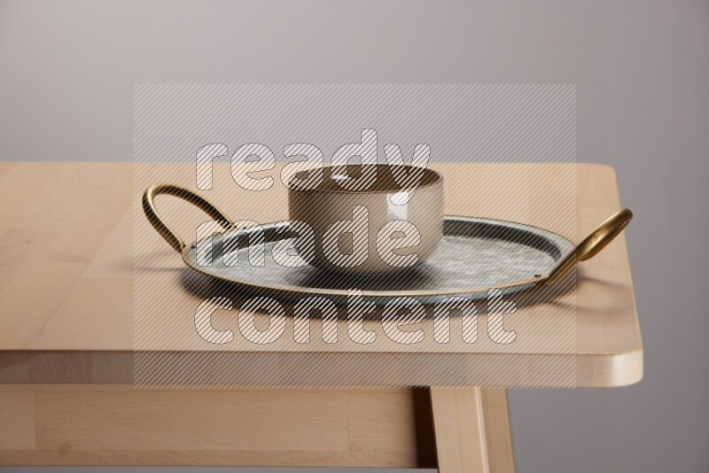 multicolored bowl placed on a rounded stainless steel tray with golden handels on the edge of wooden table