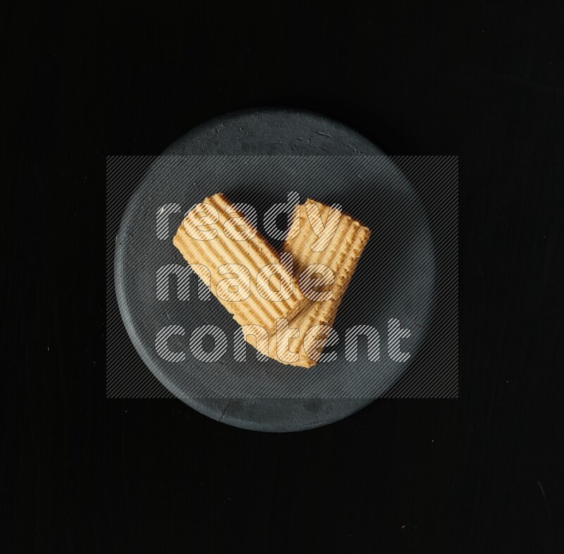 Golden biscuits in a black pottery plate on black background