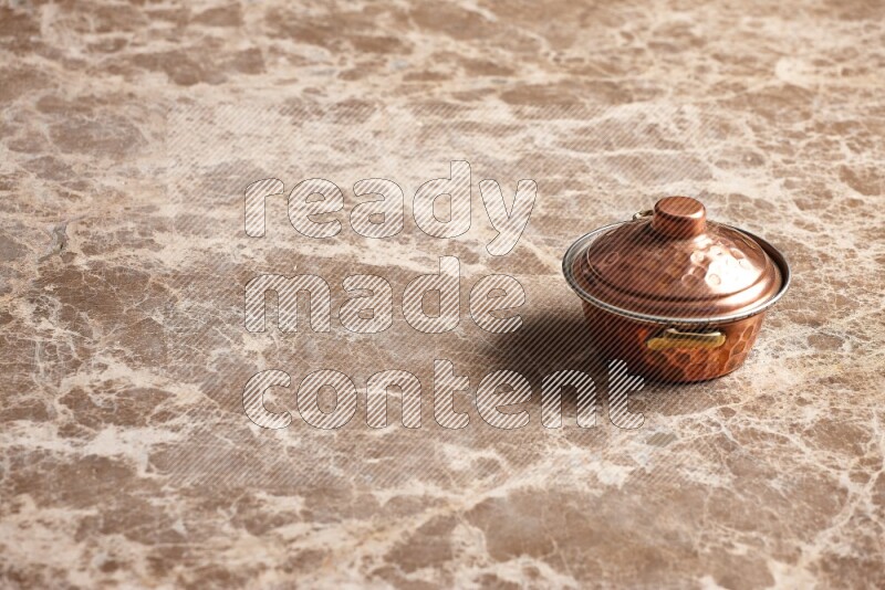 A small copper pot on beige marble background
