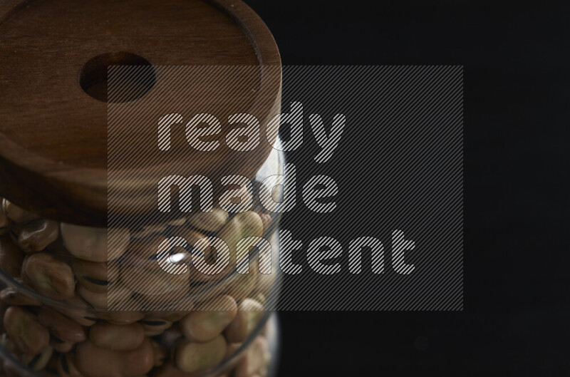 Fava beans in a glass jar on black background