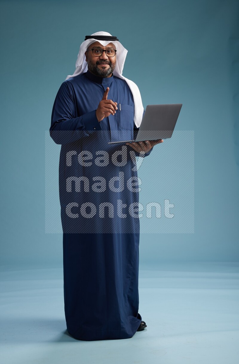 Saudi Man with shimag Standing working on laptop on blue background