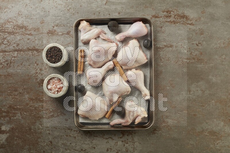 Mixed fresh chicken pieces in an oven tray on a textured rustic background