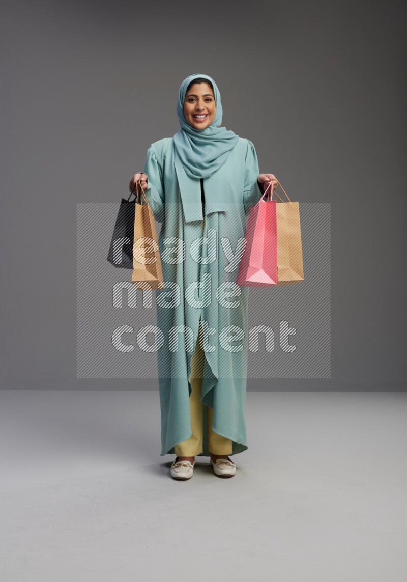 Saudi Woman wearing Abaya standing holding shopping bag on Gray background