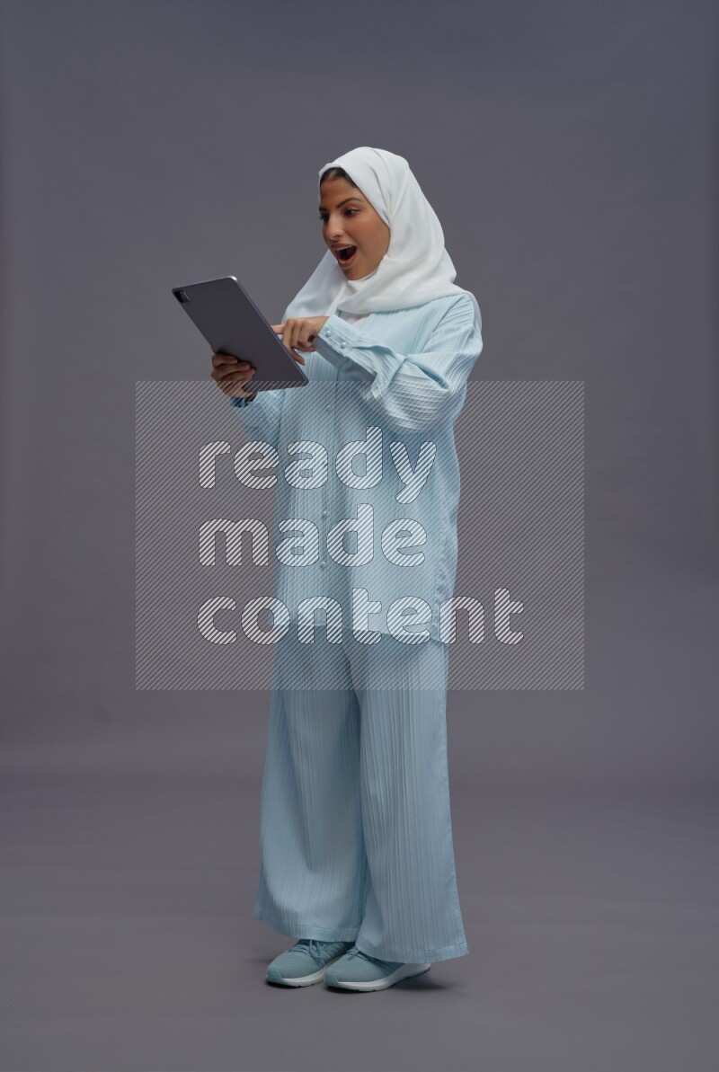 Saudi woman wearing hijab clothes standing working on tablet on gray background