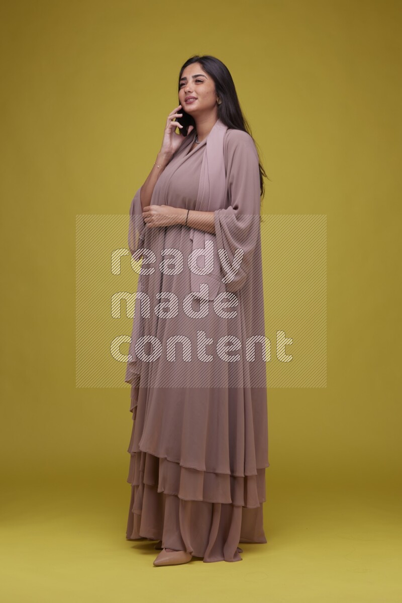 A woman Calling on a Yellow Background wearing Brown Abaya