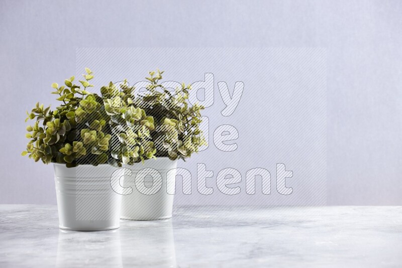 Two green artificial plants in white pot on grey marble background