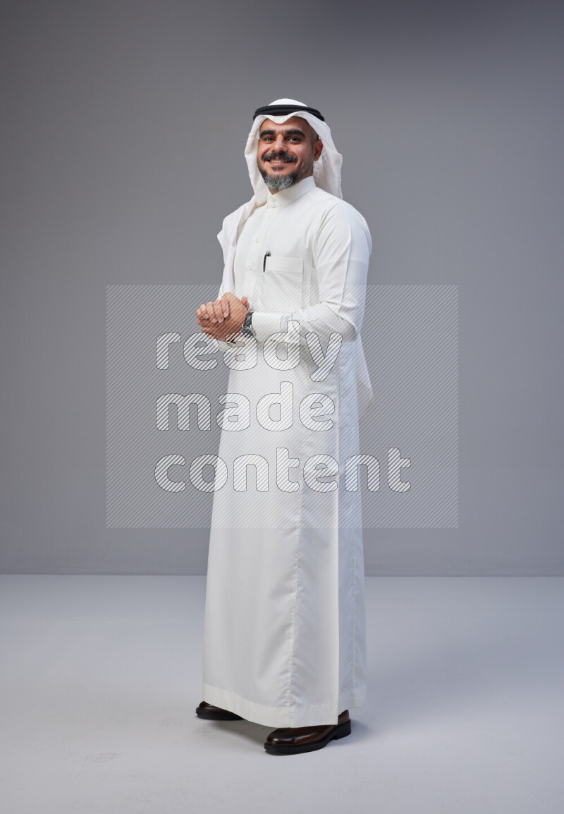 Saudi man Wearing Thob and white Shomag standing interacting with the camera on Gray background
