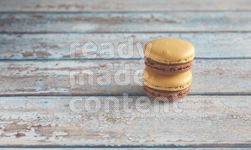 45º Shot of two Yellow and Brown Chai Latte macarons on light blue wooden background
