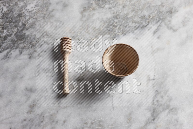 Multicolored pottery bowl with wooden honey dipper on the side on grey marble background