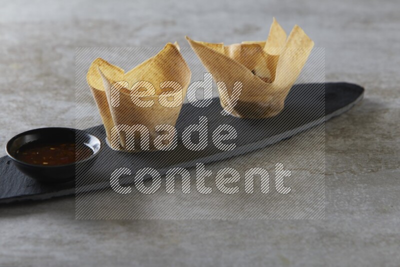 wonton cups with soy sauce ramkin on oval slate on grey textured counter top