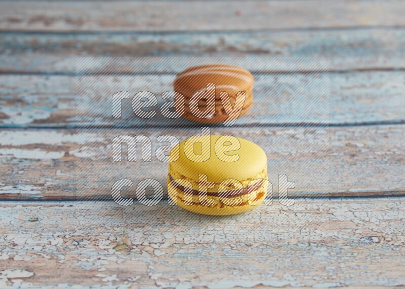45º Shot of of two assorted Brown Irish Cream, and Yellow Lemon macarons on light blue background