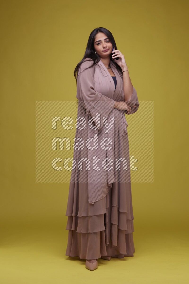 A woman Calling on a Yellow Background wearing Brown Abaya