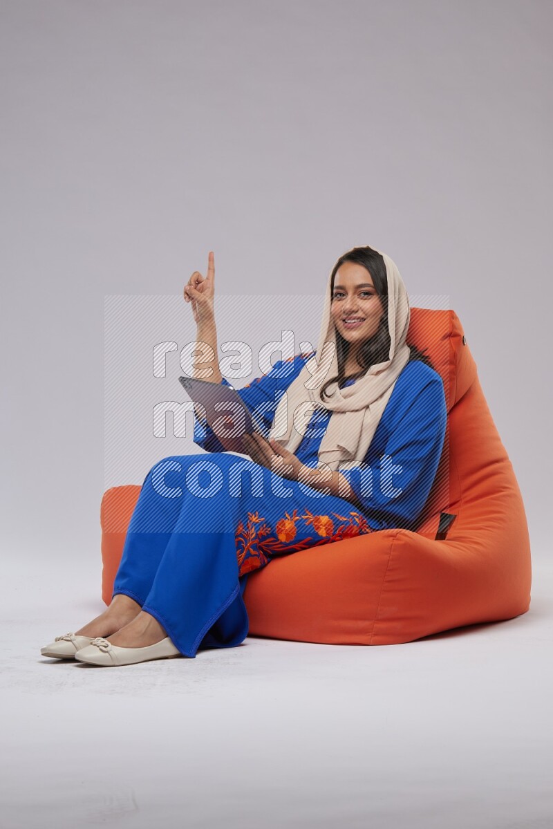 A Saudi woman sitting on an orange beanbag and working on tablet