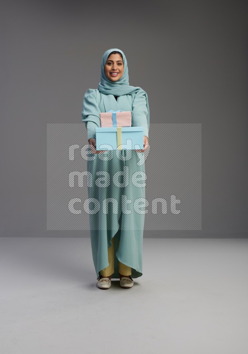 Saudi Woman wearing Abaya standing holding gift box on Gray background