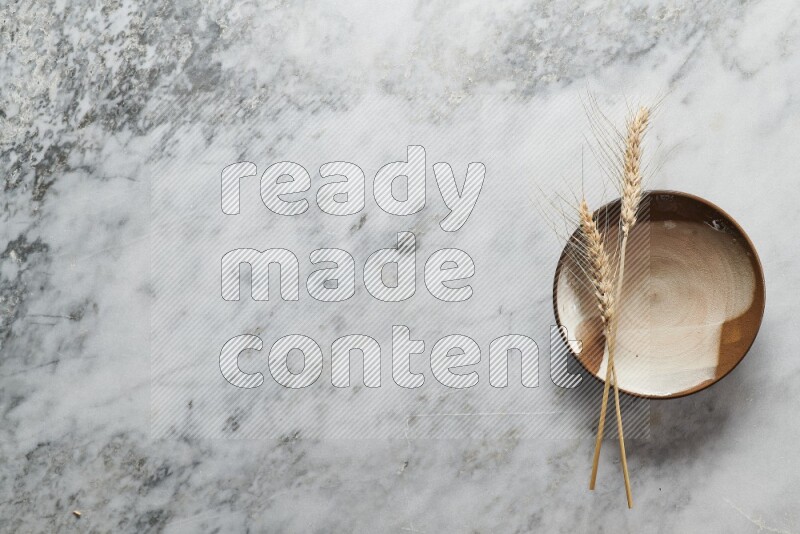 Wheat stalks on multicolored pottery plate on grey marble background