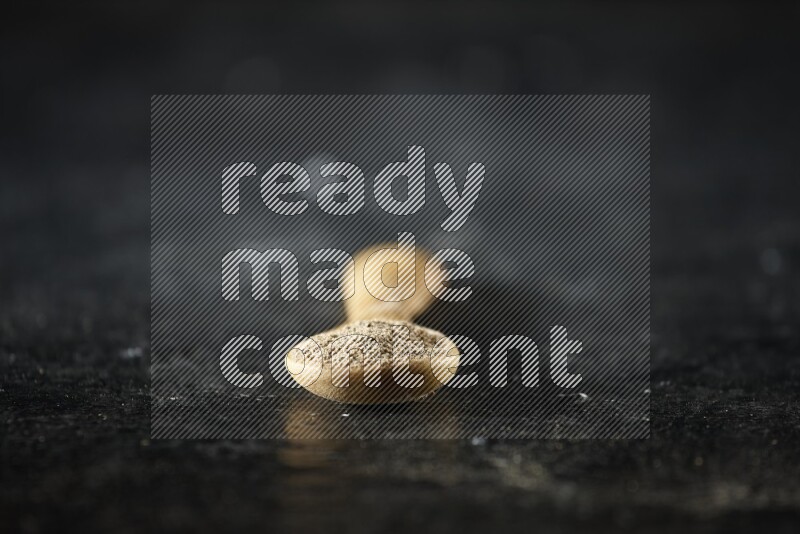 A wooden spoon full of cardamom powder on textured black flooring