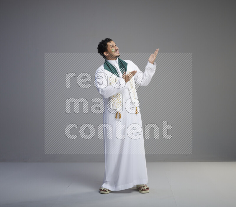 رجل سعودي يرتدي ثوب ابيض يضع شال مكتوب عليه المملكة العربية السعودية حول رقبته