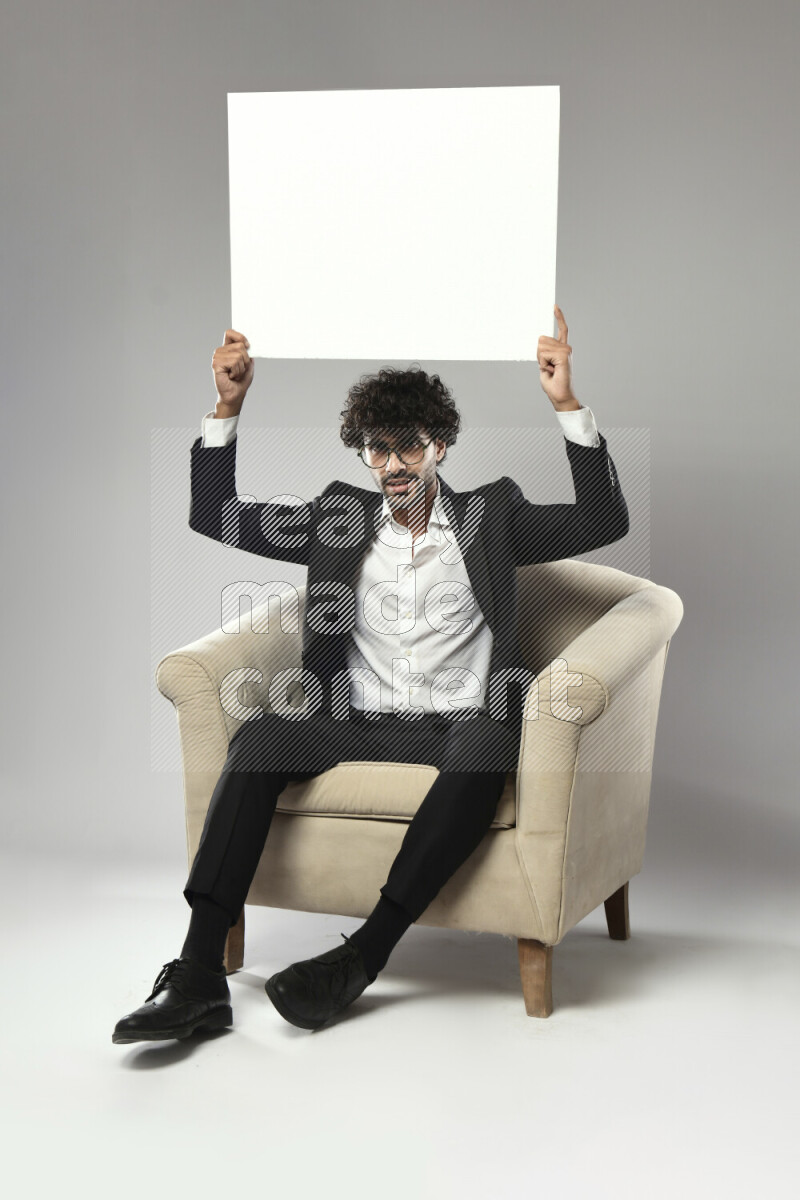 A man wearing formal sitting on a chair holding a white board on white background