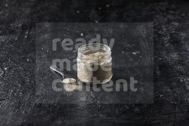 وعاء زجاجي وملعقة معدنية ممتلئان ببودرة الفلفل الأبيض على أرضية سوداء