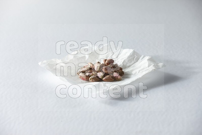 Peeled pistachios on a crumpled piece of paper on a white background in different angles
