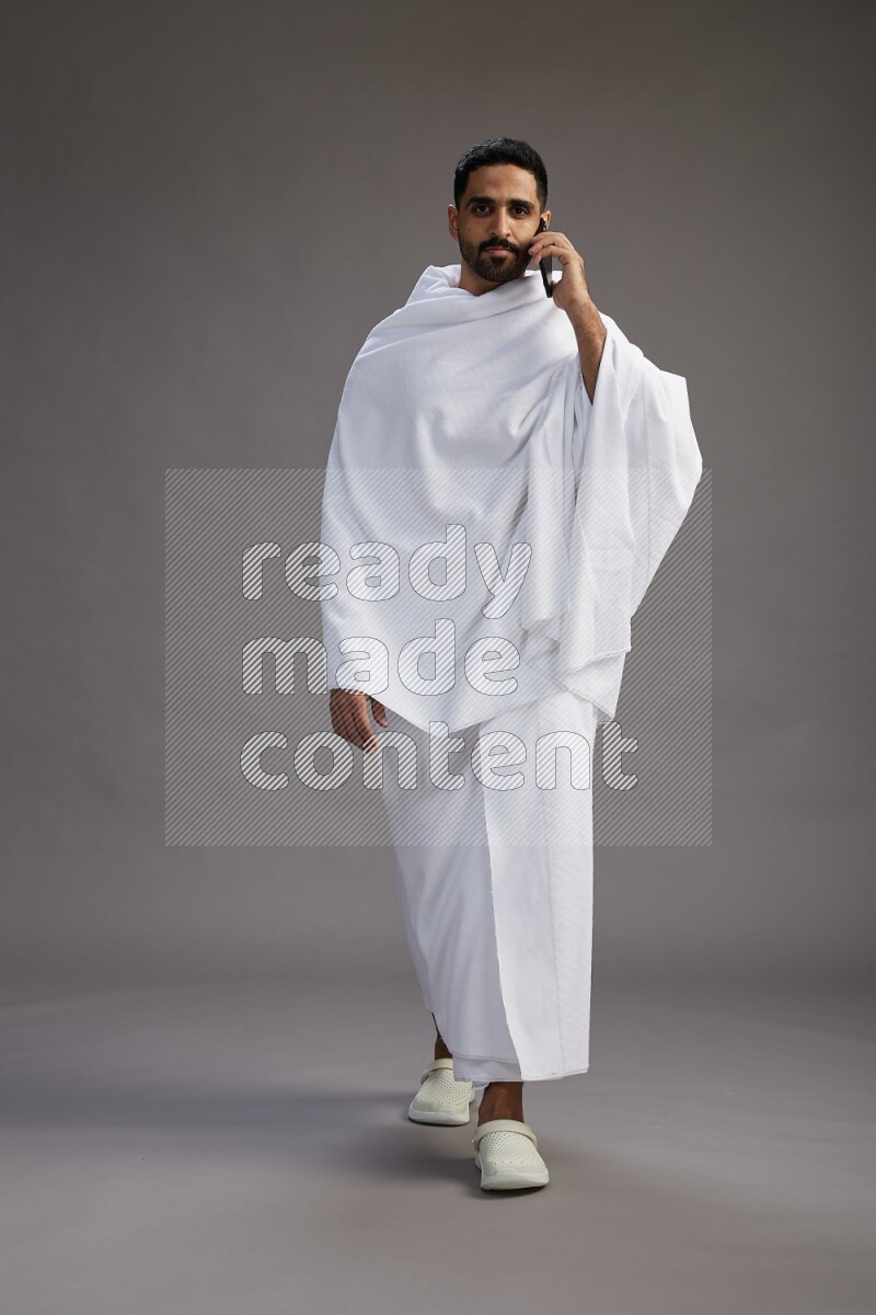 A man wearing Ehram Standing talking on phone on gray background
