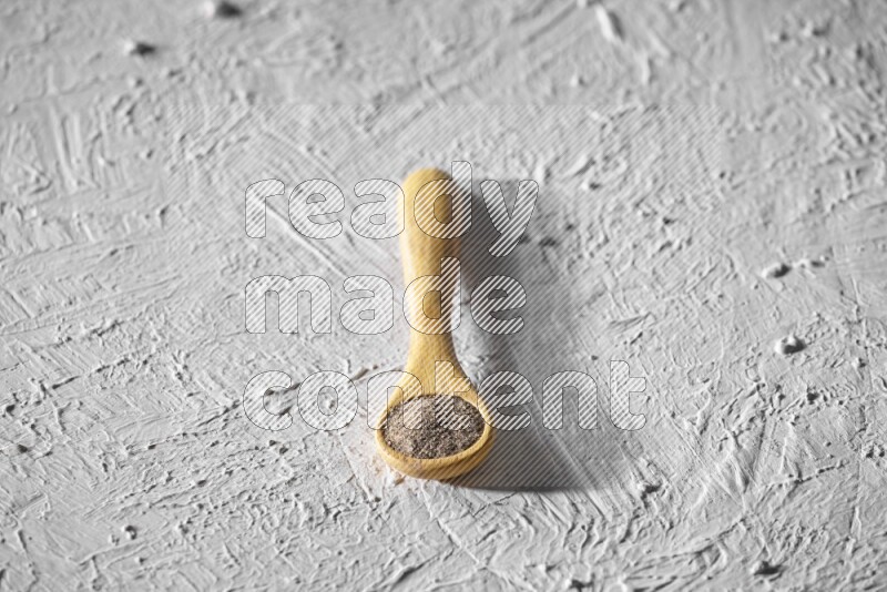 A wooden spoon full of black pepper powder on a textured white flooring