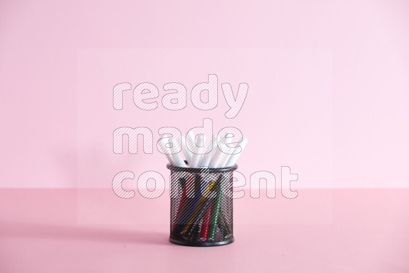 Pens, pencils and other different school supplies in a metal pen holder on rose background